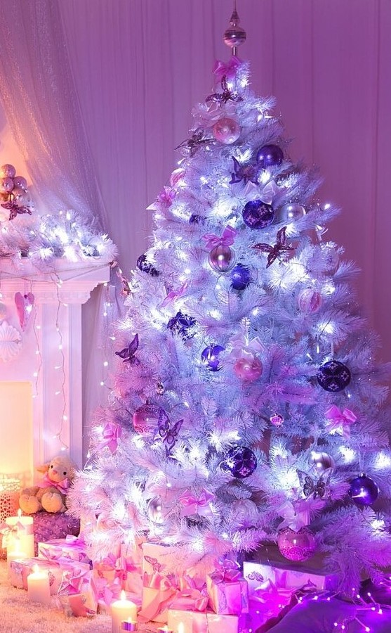 a white Christmas tree with pink and purple ornaments, lights and a tree topper plus candles around is amazing