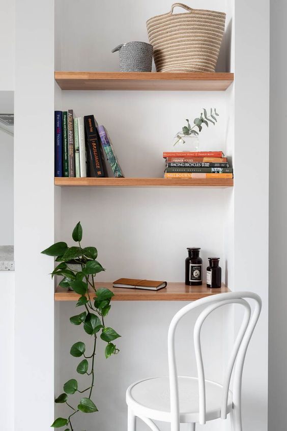 a tiny home office nook with several built-in shelves and a desk, a white chair and a potted plant just to make some notes or pay some bills