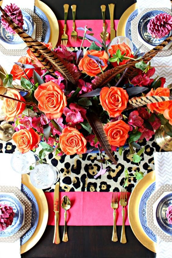 a super bold Thanksgiving tablescape with blue and gold plates, a leopard and hot pink table runner, orange blooms and feathers