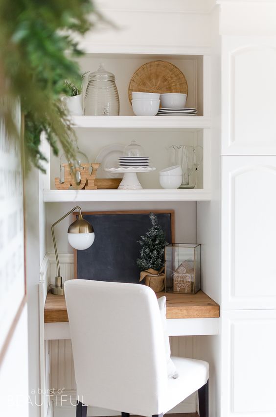 a tiny home office space in the kitchen, with just a small built in desk, a white chair and a brass lamp plus a chalkboard