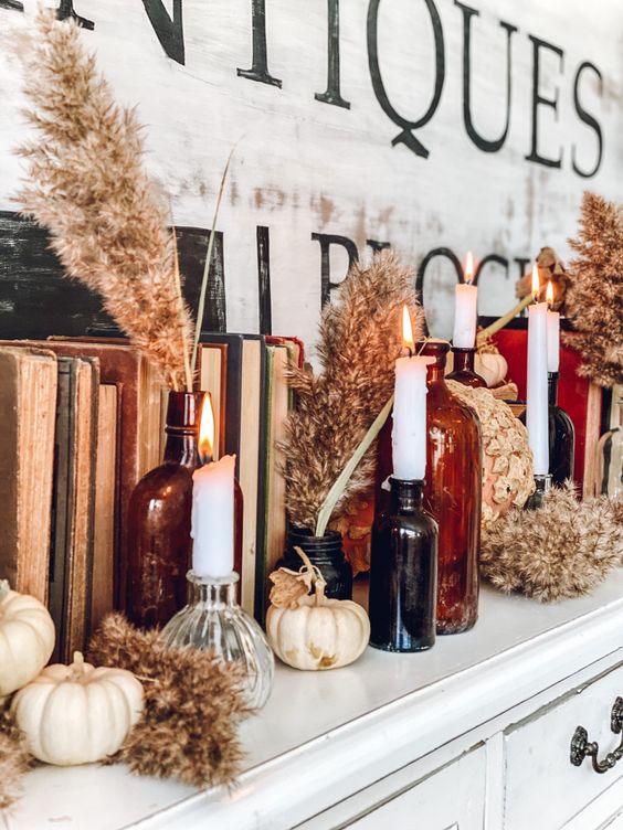 boho Thanksgiving decor with neutral pumpkins and dried blooms, white candles in dark apothecary bottles and vintage books
