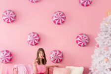 32 a pink holiday space with peppermints on the wall, pink furniture and balloon and pink ornaments on a white Christmas tree