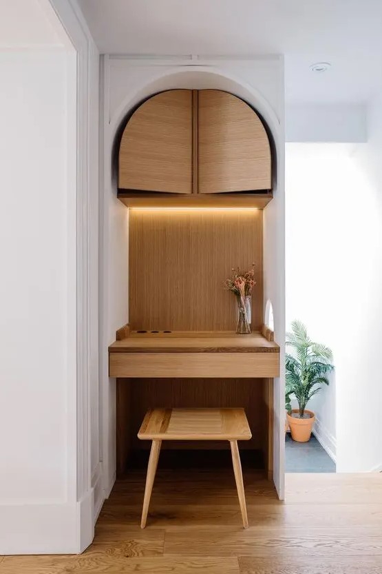 a tiny nook turned into a working space clad with plywood, with a storage unit and a built-in desk, a stool and built-in lights