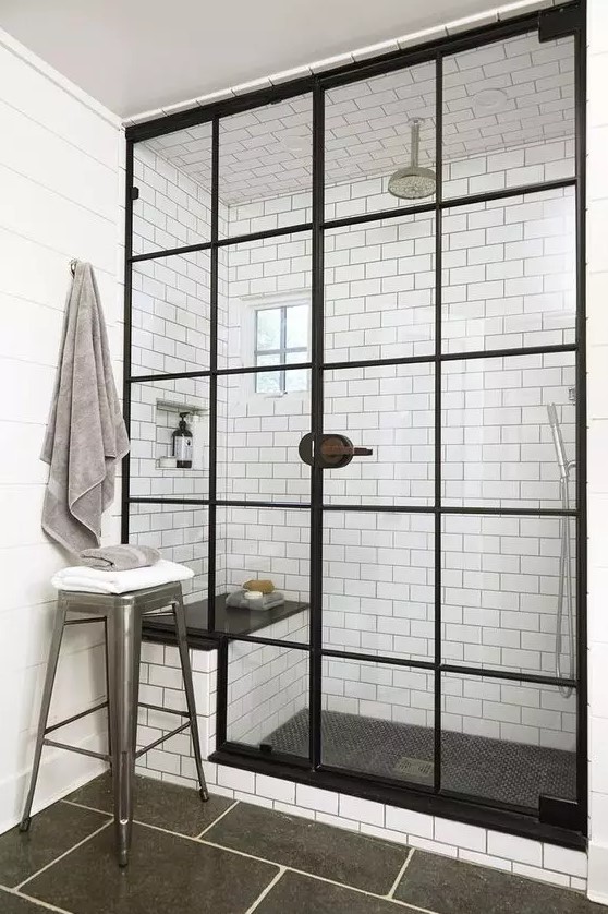 a vintage inspired bathroom with white subway and graphite grey tiles, a shower space with black frame doors and a bench inside