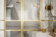 33 an exquisite bathroom clad with white marble tiles and a vanity, a shower space with glass and gold doors and gold fixtures