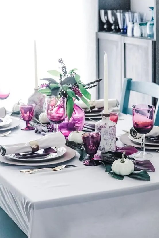 a stylish modern Thanksgiving tablescape with foliage on the table, a purple vase with purple blooms, purple glasses and all the rest done in neutrals