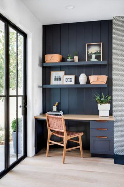 a little navy home office nook in the kitchen, with shiplap on the wall, a stylish desk, some shelves and a woven chair plus potted plants