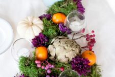 38 an eye-catchy Thanksgiving centerpiece with moss, white pumpkins, artichokes, berries, citrus and some candles plus purple blooms