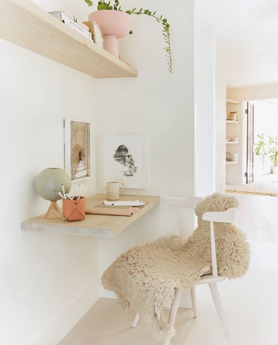 a small and airy working nook with a floating shelf, a floating desk, a chair with faux fur and some lovely decor