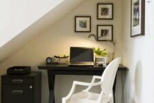41 a small attic nook with a trestle black desk and a file cabinet, a white chair, a small gallery wall and a table lamp