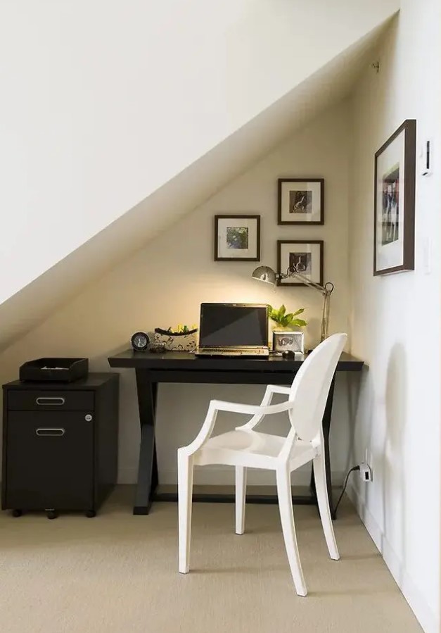 a small attic nook with a trestle black desk and a file cabinet, a white chair, a small gallery wall and a table lamp