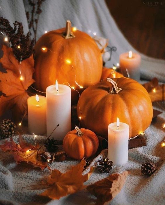 Thanksgiving decor with bold orange faux pumpkins and leaves, pinecones, LED lights, candles is a very cozy idea