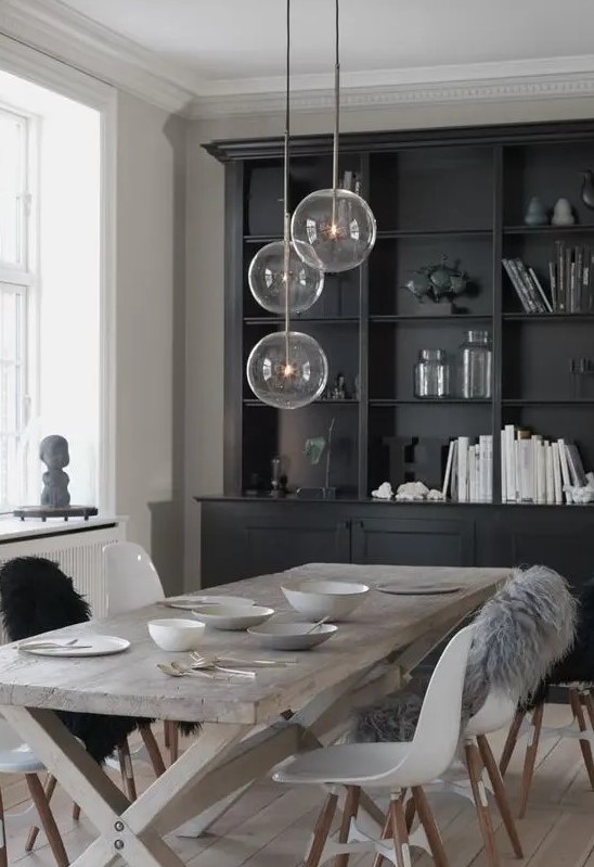 a Nordic dining space with a black storage unit, a reclaimed trestle dining table, matching white chairs and pendant lamps