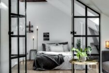 a Scandinavian bedroom in black and white, with a simple bed, floor lamps, dark wooden beams and a glass framed door