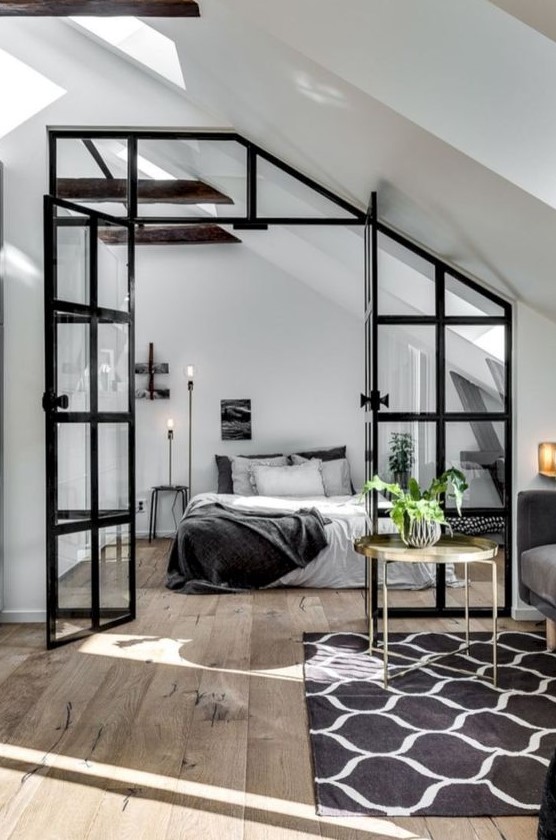 a Scandinavian bedroom in black and white, with a simple bed, floor lamps, dark wooden beams and a glass framed door