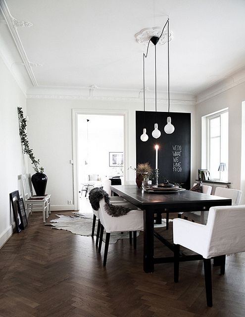 a Scandinavian dining room with a black accent wall, a black dining table, white chairs, pendant bulbs, a large black vase