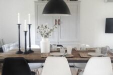 a Scandinavian dining space with a stained table, black and white chairs, a grey storage unit and a black pendant lamp