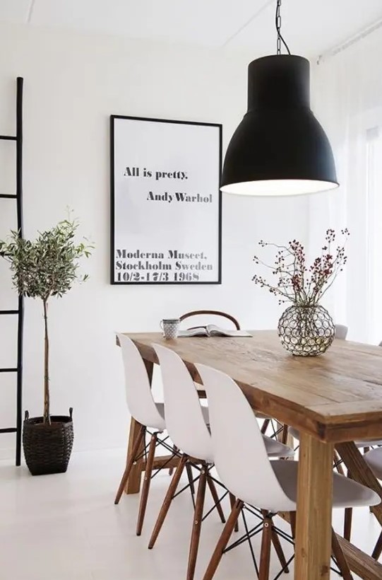 a beautiful Scandinavian dining room with a light-stained wooden table, matching white chairs, a statement black pendant lamp and an artwork