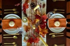 a beautiful Thanksgiving table with orange napkins, bold leaves, pinecones, neutral candles and pumpkins