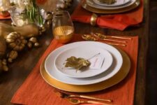 a beautiful Thanksgiving tablescape with orange placemats and napkins, gold glasses, chargers and cutlery plus gilded veggies