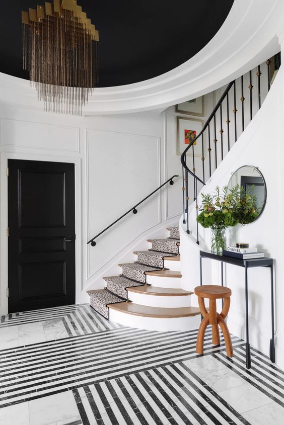 a beautiful black and white entryway with black doors and a ceiling, a black and white marble floor, a black console table and a gorgeous chandelier