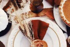 a beautiful boho Thanksgiving tablescape with terracotta napkins, dried citrus slices, wheat and grasses, rust glasses