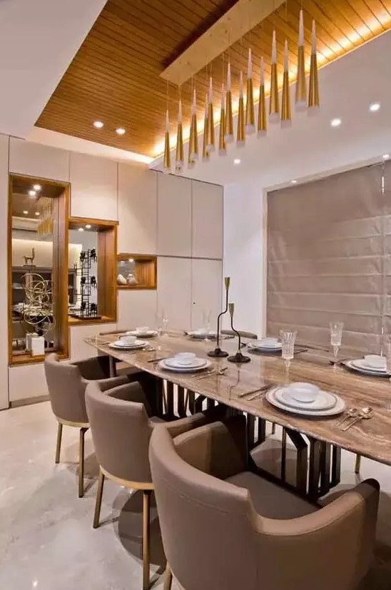 a beautiful contemporary dining room with built-in and pendant lamps, with a long table and taupe chairs, a storage unit with mirrors
