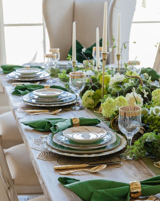 a beautiful emerald and gold Thanksgiving tablescape with fresh green blooms and greenery, tall and thin candles, emerald plates and napkins