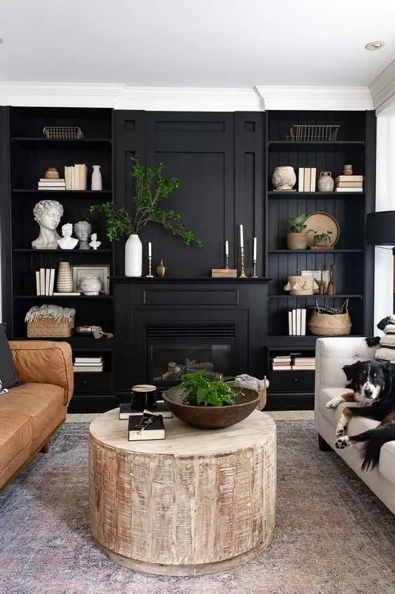 a beautiful farmhouse living room with a black accent wall with shelves and a built in fireplace, a couple of sofas and a round tree stump coffee table