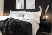 a black and white Scandinavian bedroom with a black accent wall, a bed with black and white bedding, a black nightstand and lights