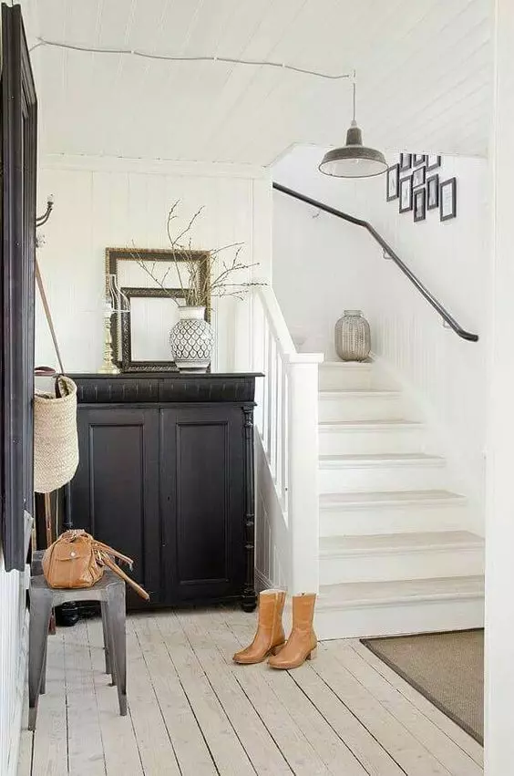 a black and white entryway with a black built in cabinet, artworks, metal stools, empty frames and a pendant lamp
