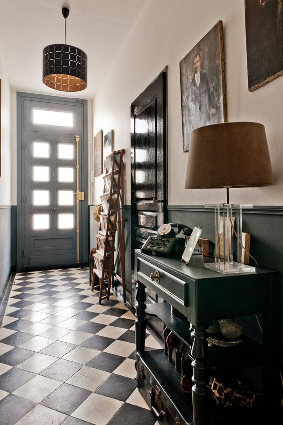 a black and white entryway with a black vintage console table, a ladder for storage, a pendant and a floor lamp and an artwork