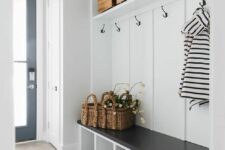 a black and white farmhouse mudroom with a built-in shelf, a bench, baskets and boxes and a black door