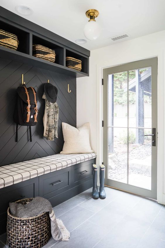 a black and white farmhouse mudroomw ith a black accent wall and built-in storage units, a basket for storage and a glass door