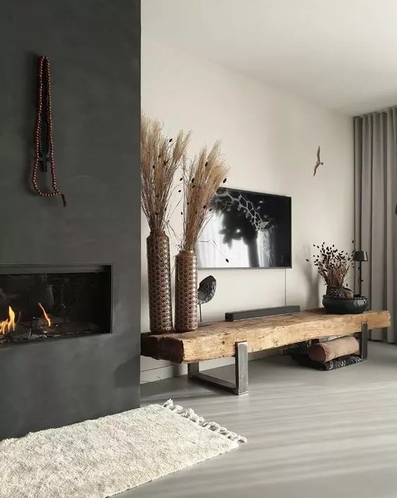 a boho monochromatic living room with a built in fireplace, a rough wood bench, a TV on the wall and dried grass arrangements
