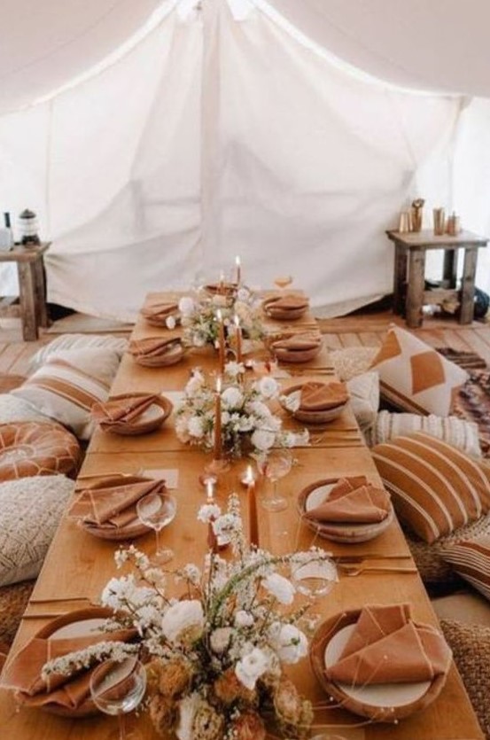 a boho Thanksgiving tablescape with terracotta linens, white blooms and rust candles plus lots of pillows