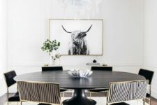 a bold and catchy black and white dining room with a round table, black and striped chairs, an artwork, a printed rug and greenery