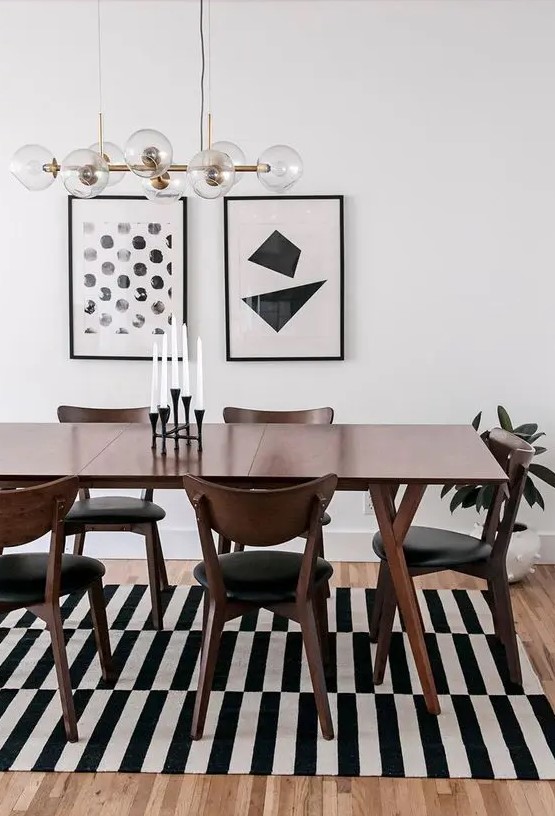 a bold black and white mid-century modern dining space with a stained table and black chairs, a striped rug and a gallery wall