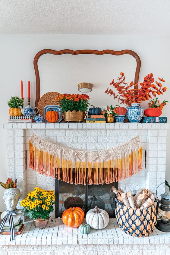 a bold fall or Thanksgiving mantel with orange blooms, pumpkins and candles, bold orange fringe and some blue vases