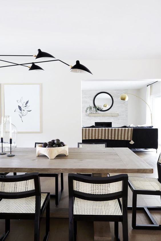 a breathtaking black and white dining room with a large stained table, neutral and black chairs, black lamps
