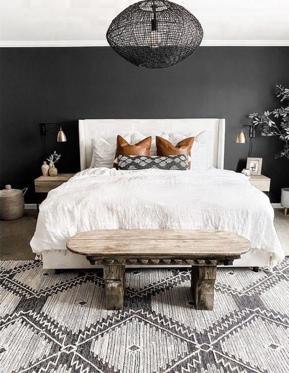 a catchy bedroom with a black accent wall, a white bed with neutral bedding, a carved wooden bench and wall mounted nightstands