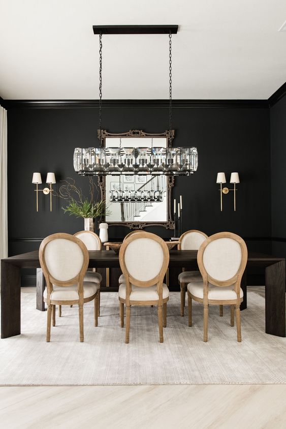 a chic and catchy black and white dining room with black walls, a dark stained dining table, neutral chairs and a beautiful chandelier