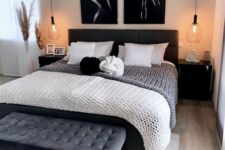 a chic and dramatic bedroom with a black bed and monochromatic bedding, a black upholstered bench, black nightstands and a chandelier