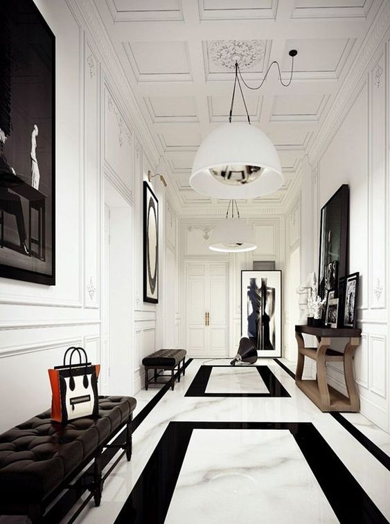 a chic black and white entrance with white walls and a marble floor, artworks and a mirror ina  frame, black leather benches