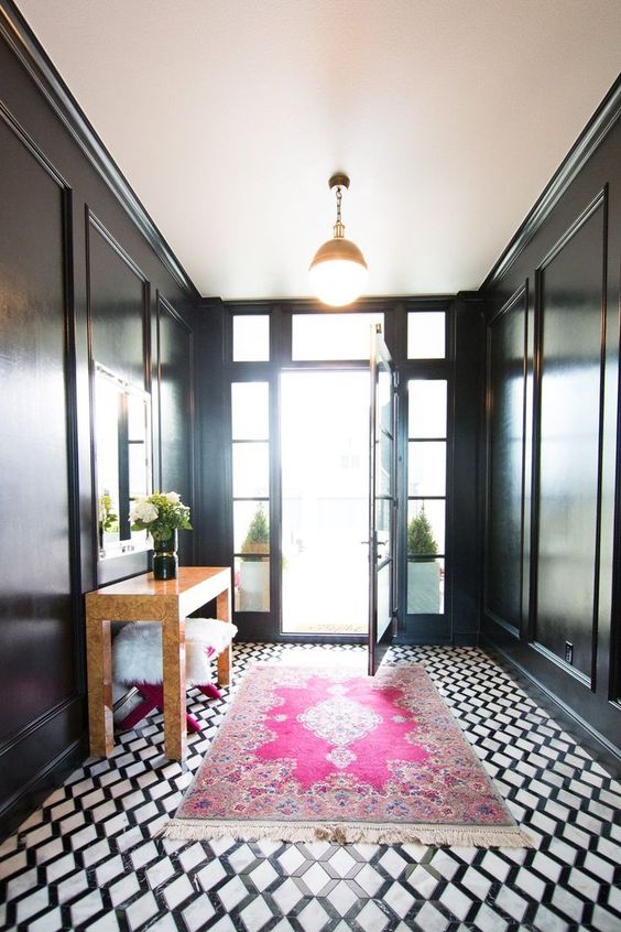 a chic entryway with black walls and doors, a black and white floor, a large mirror and a neutral console table, a bright rug