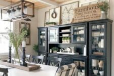a chic farmhouse dining area with a black and glass buffet, signs, a white table and checked chairs and a frame chandelier