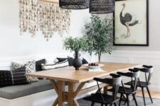 a chic modern farmhouse dining room with white paneled walls, a built-in banquette seating, a trestle dining table, black chairs and black woven pendant lamps