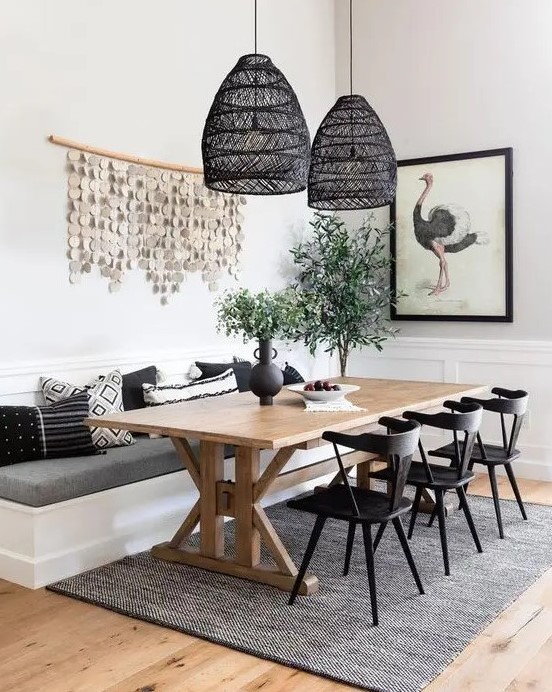 a chic modern farmhouse dining room with white paneled walls, a built in banquette seating, a trestle dining table, black chairs and black woven pendant lamps