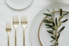 a clean and minimal Thanksgiving place setting with white porcelain, gold cutlery, a color block gold vase with grasses
