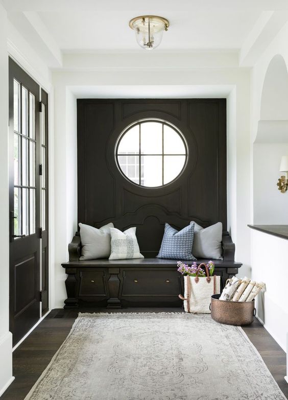 a cozy black and white mudroom with a black accent wall, a porthole window and a built-in bench, neutral pillows and a grey rug